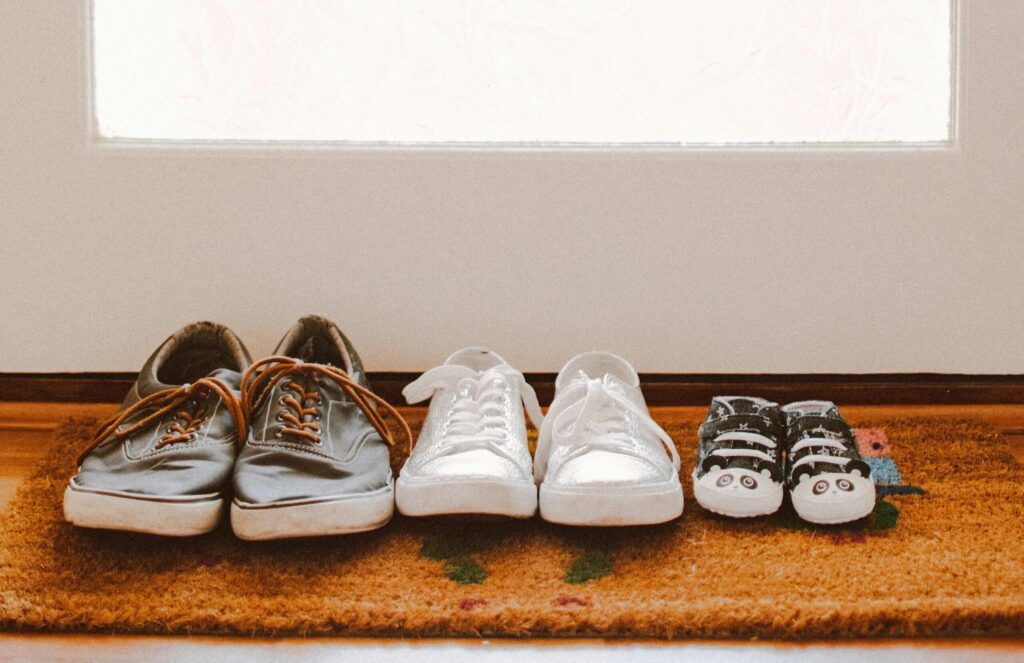 A collection of family shoes, including baby booties, on a welcoming mat by the door.